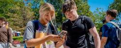 Picture of students talking and looking at a mobile phone.